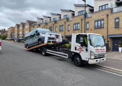 A tow truck is towing a van down a street.