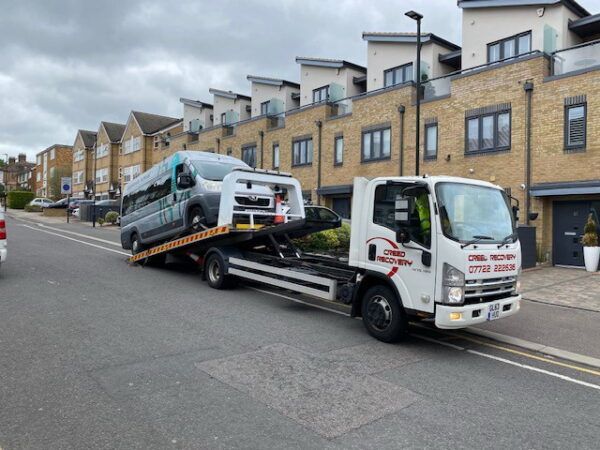 A tow truck is towing a van down a street.