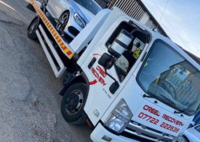 A white tow truck is parked next to a white car.