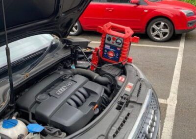 A red car is parked next to a black car with the hood open.