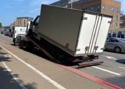 A white truck is being towed down a street by a tow truck.