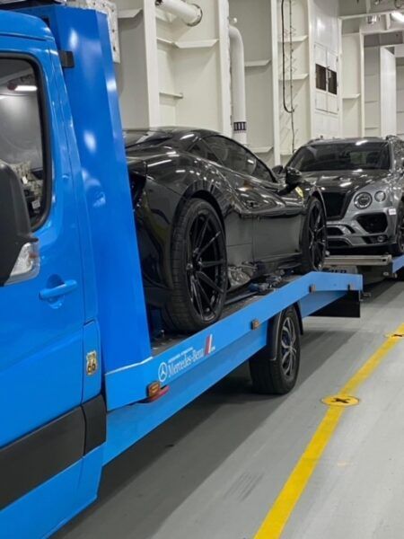 A blue tow truck is carrying a black sports car