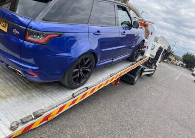 A blue range rover sport is being towed by a tow truck.