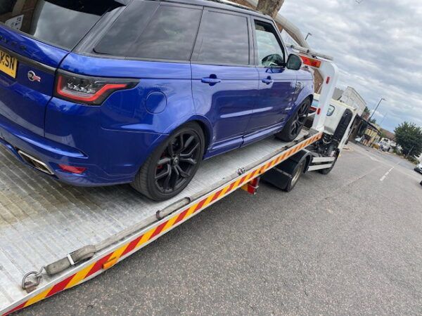 A blue range rover is being towed by a tow truck.