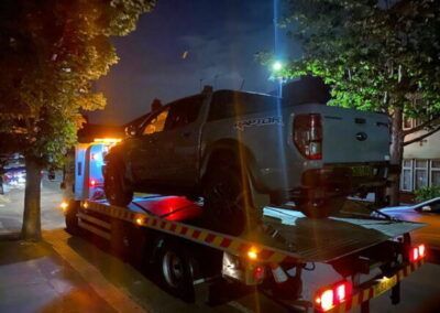 A truck is being towed down a street at night.