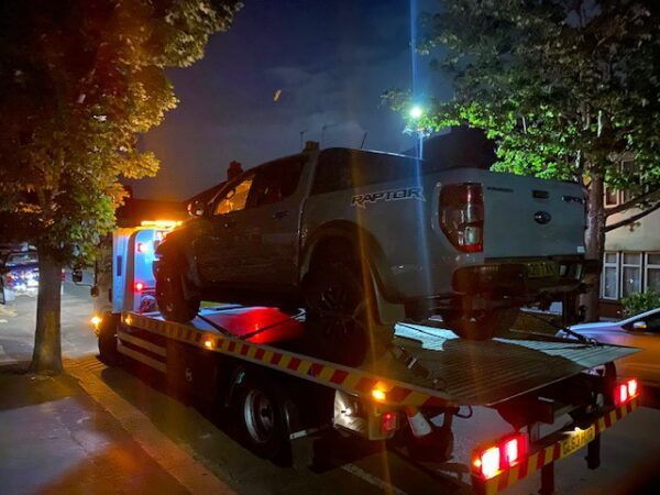 A truck is being towed down a street at night.