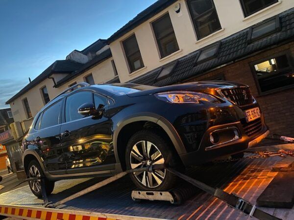 A black car is sitting on top of a tow truck.