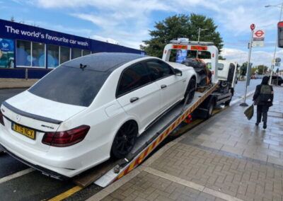 A white mercedes benz is being towed by a tow truck.