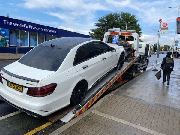 A white car is being towed by a tow truck.
