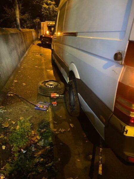 A white van is parked on the side of the road with a flat tire.