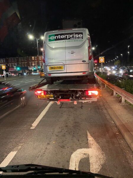 A van is being towed down a highway by a tow truck.