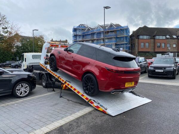 A red car is being towed by a tow truck in a parking lot.