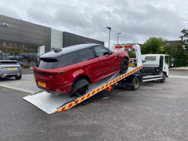 A red range rover is being towed by a tow truck.