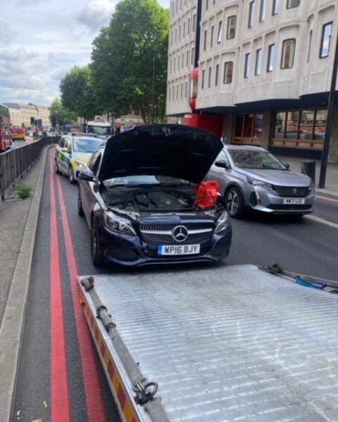 A car with the hood up is being towed by a tow truck