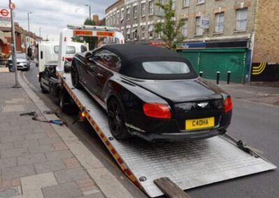 A black bentley convertible is being towed by a tow truck.