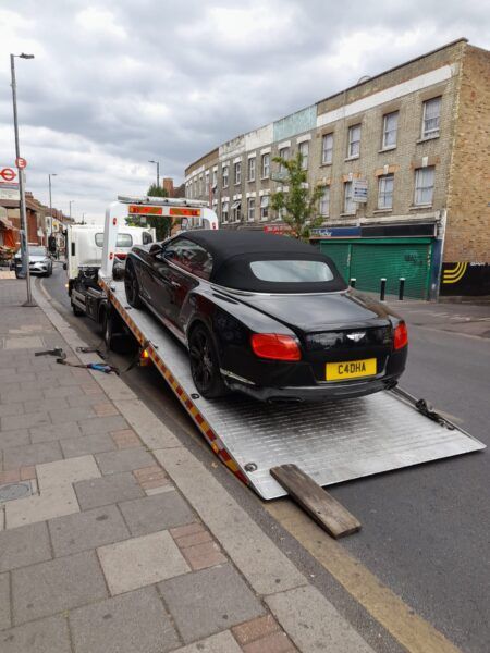 A bentley convertible is being towed down the street