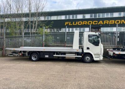 A flatbed tow truck is parked in front of a building.
