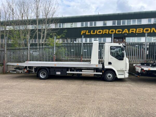 A flatbed tow truck is parked in front of a building that says fluorocarbon.