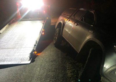A car is being towed by a tow truck at night.