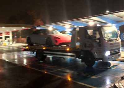A tow truck is towing a car in a parking lot at night.