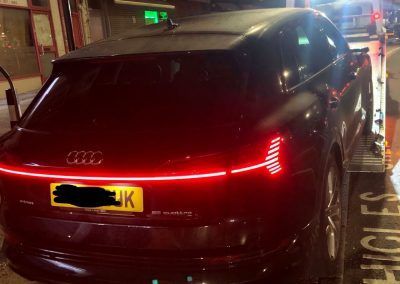 A black car with a license plate that says uk is being towed by a tow truck.