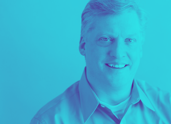 A man in a blue shirt is smiling and looking at the camera.