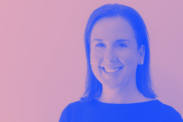 A woman in a black shirt is smiling in front of a pink background.