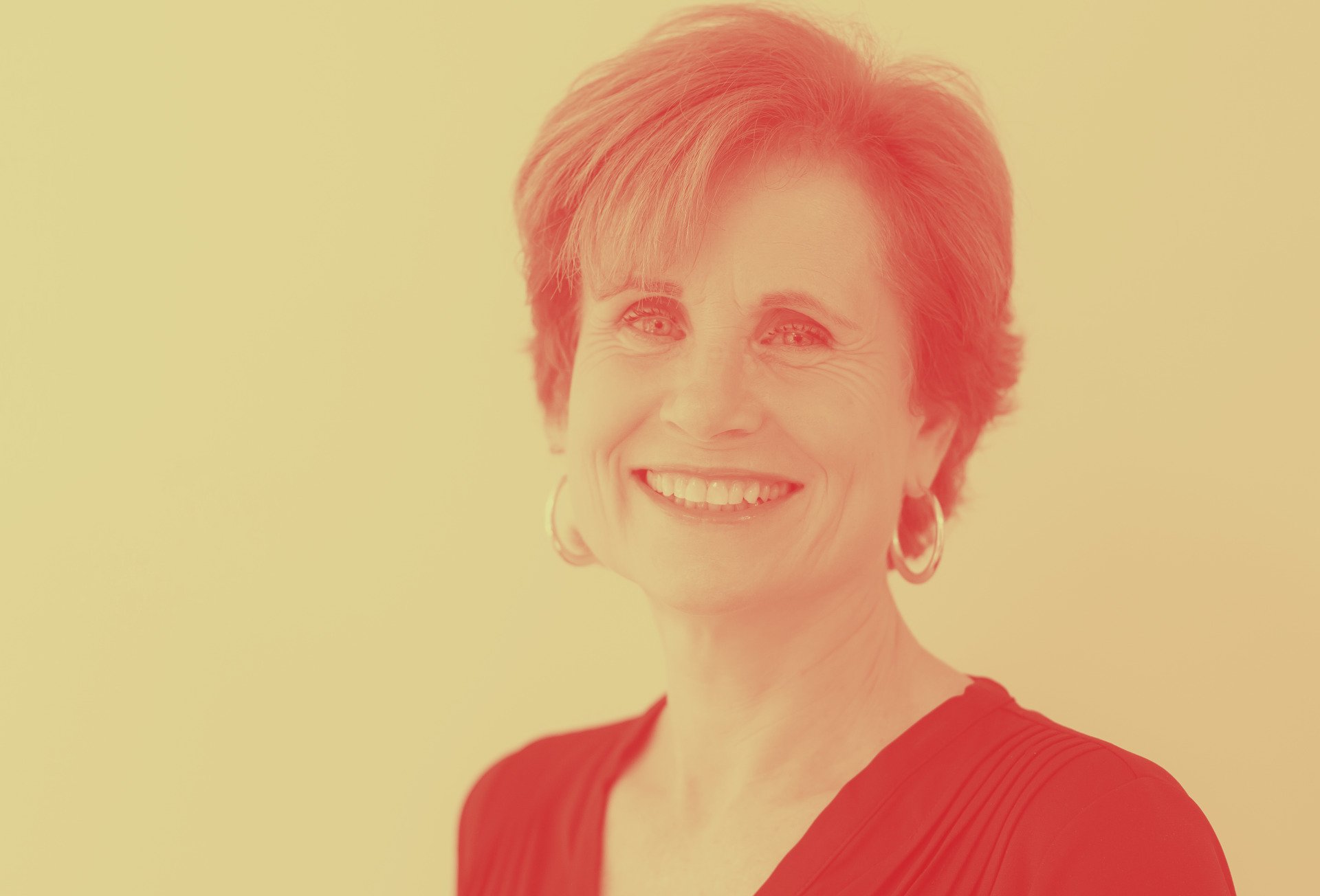A woman in a red shirt and earrings is smiling for the camera.
