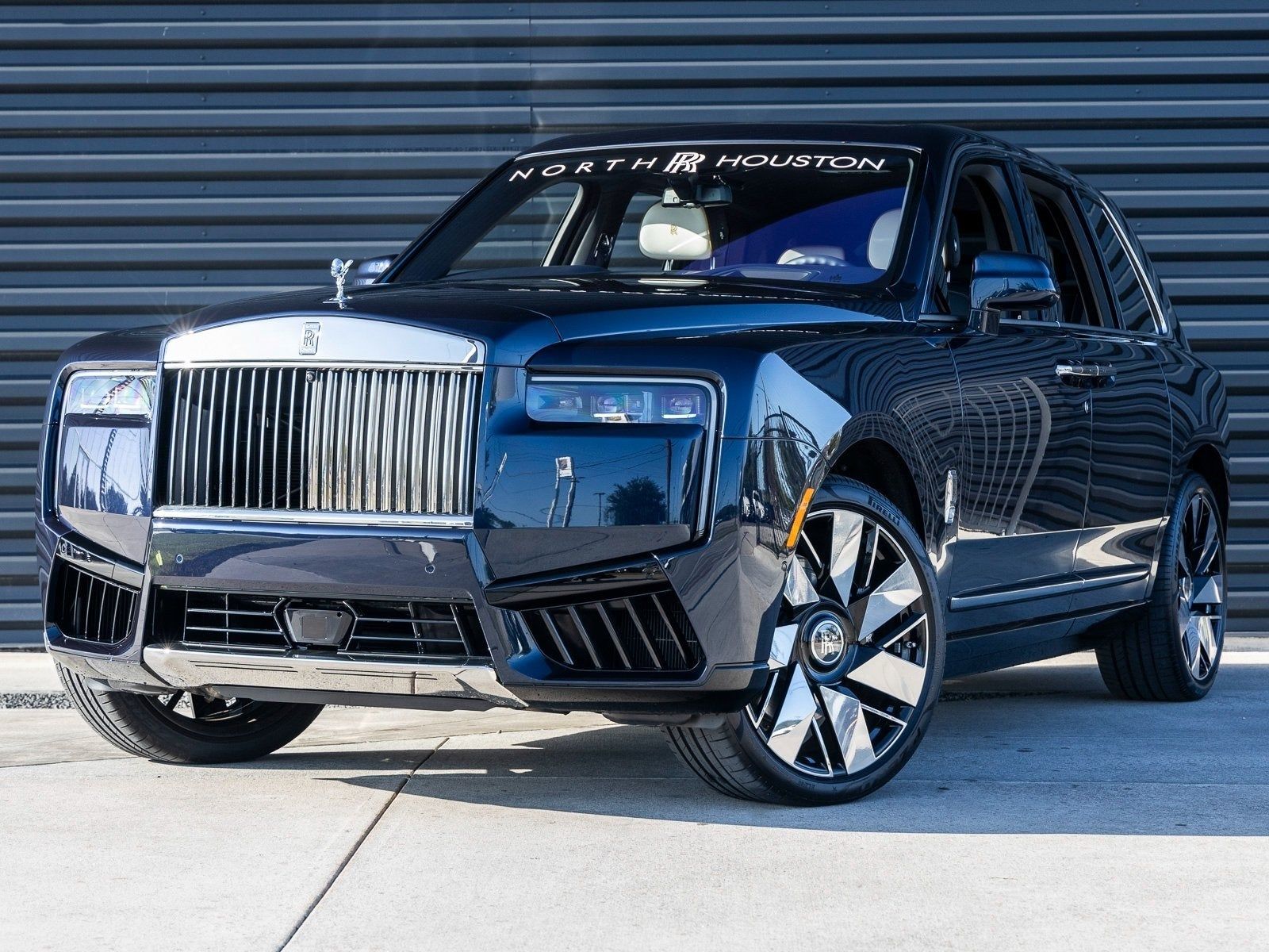 A rolls royce cadillac cullinan is parked in front of a building.