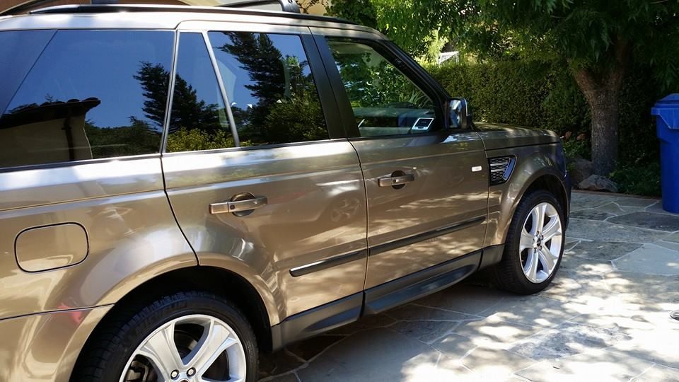 A range rover sport is parked in a driveway next to a trash can.