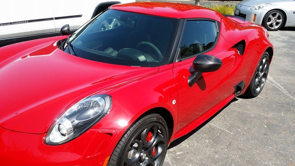 A red sports car is parked in a parking lot next to a silver car.