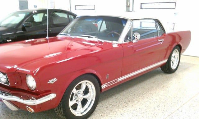 A red mustang is parked in a garage next to a black car