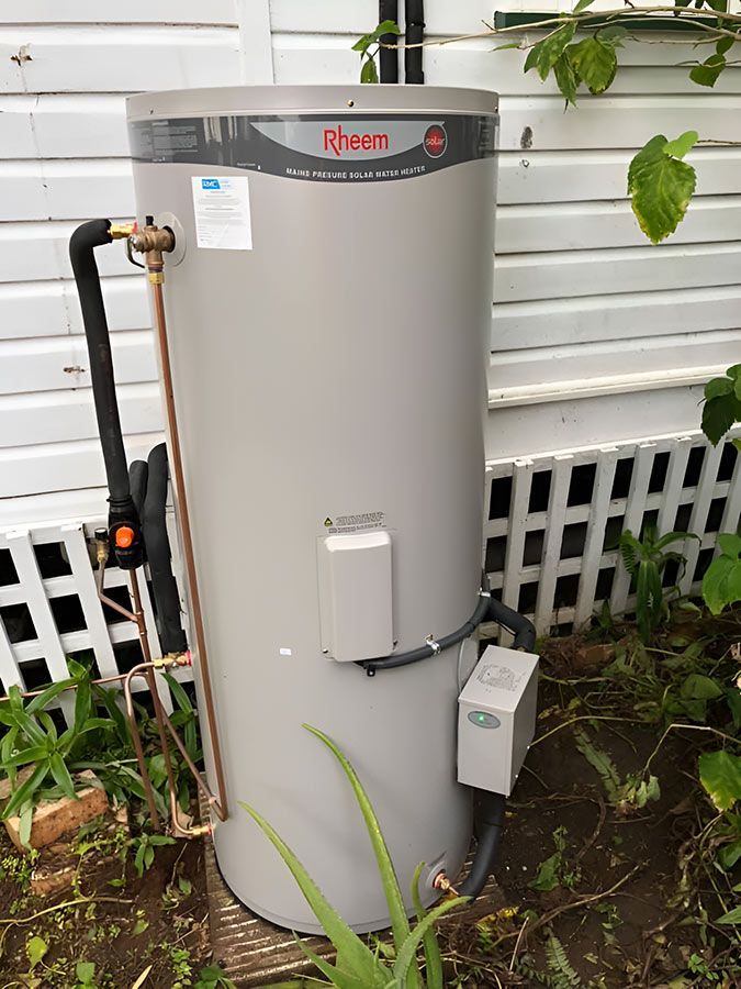 A Hot Water System Is Sitting In Front Of A White House — No Risk Plumbing Kyogle Pty Ltd in Geneva, NSW