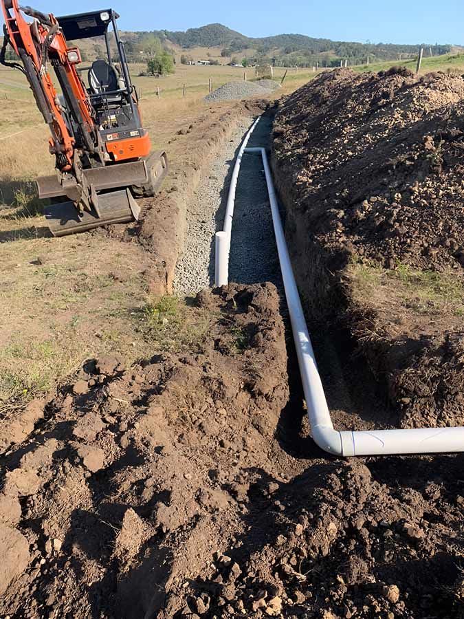 A Small Excavator Is Digging A Trench In The Dirt — No Risk Plumbing Kyogle Pty Ltd in Geneva, NSW
