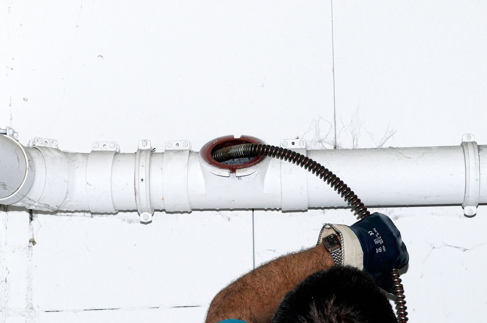 A Man Is Unclogging A Drainage Pipe — No Risk Plumbing Kyogle Pty Ltd in Geneva, NSW