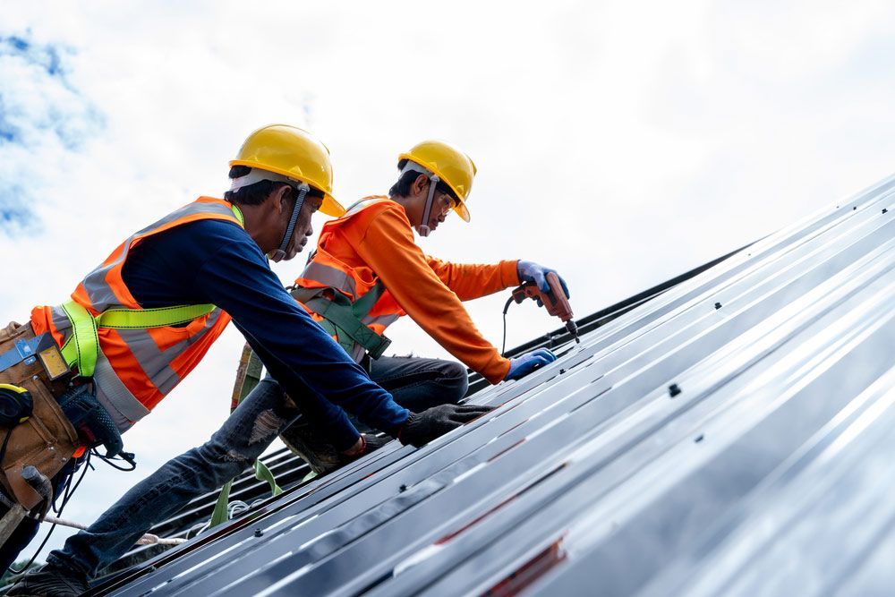 Two Construction Workers Are Working On The Roof Of A Building — No Risk Plumbing Kyogle Pty Ltd in Geneva, NSW