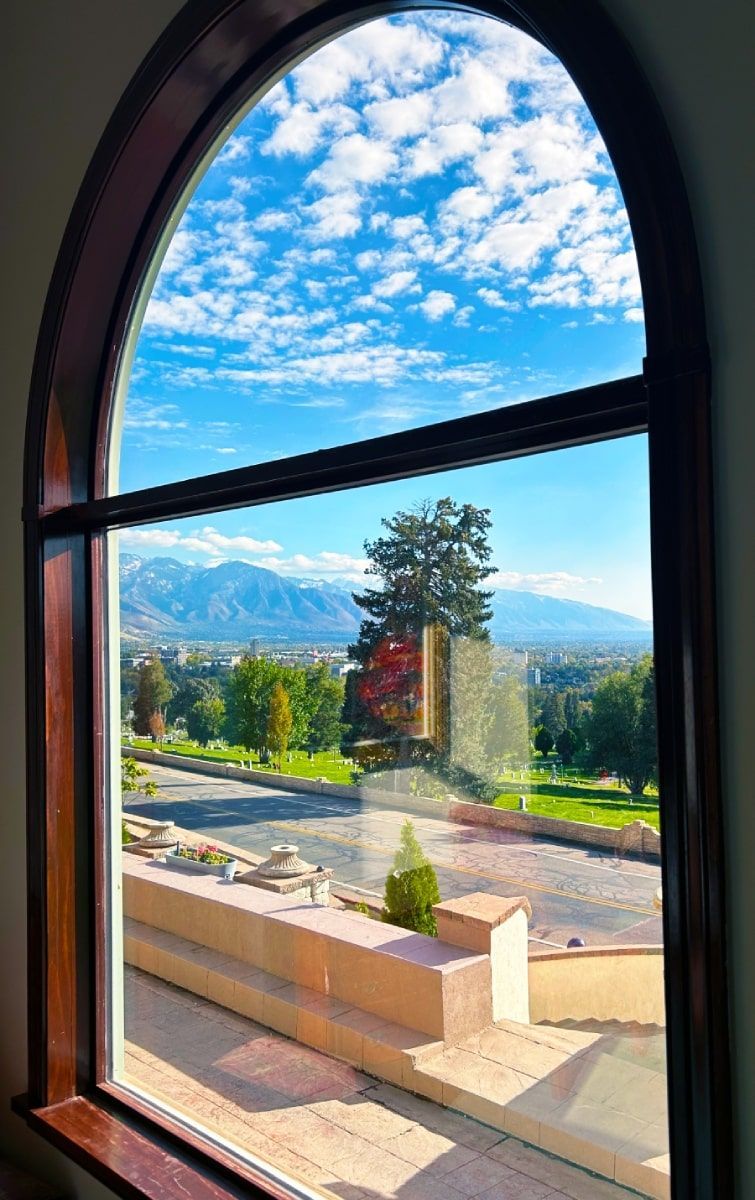 Arched window view of a sunny city, mountains, and partly cloudy sky.