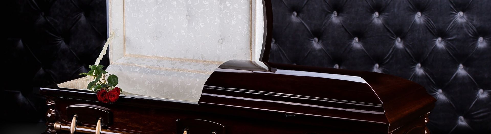 A dark brown coffin with an open lid, white interior, and a red rose. Black button-tufted backdrop.
