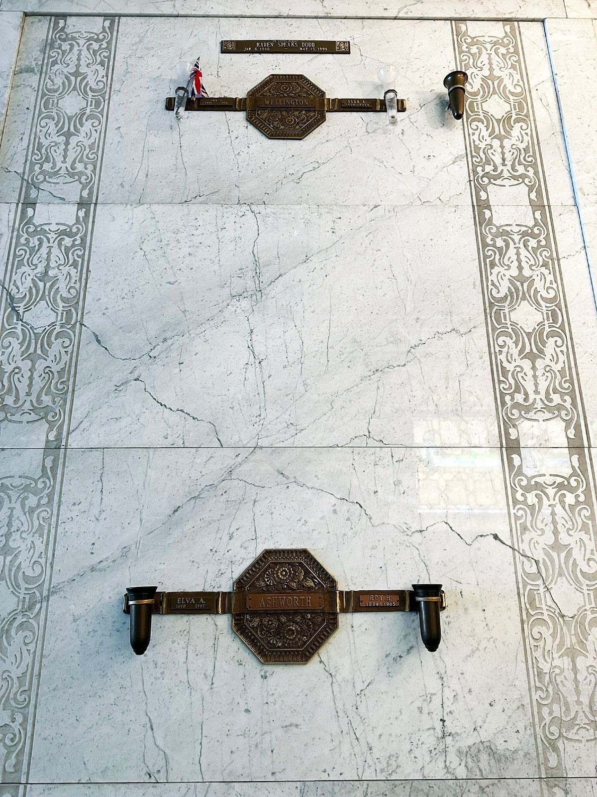 Two marble-faced crypts with bronze plaques and decorative borders in a mausoleum.