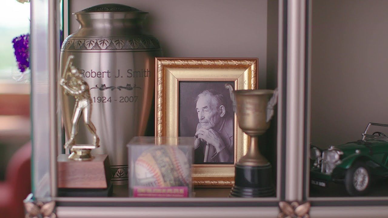 Shelf with urn, framed photo of older man, trophy, and toy car.