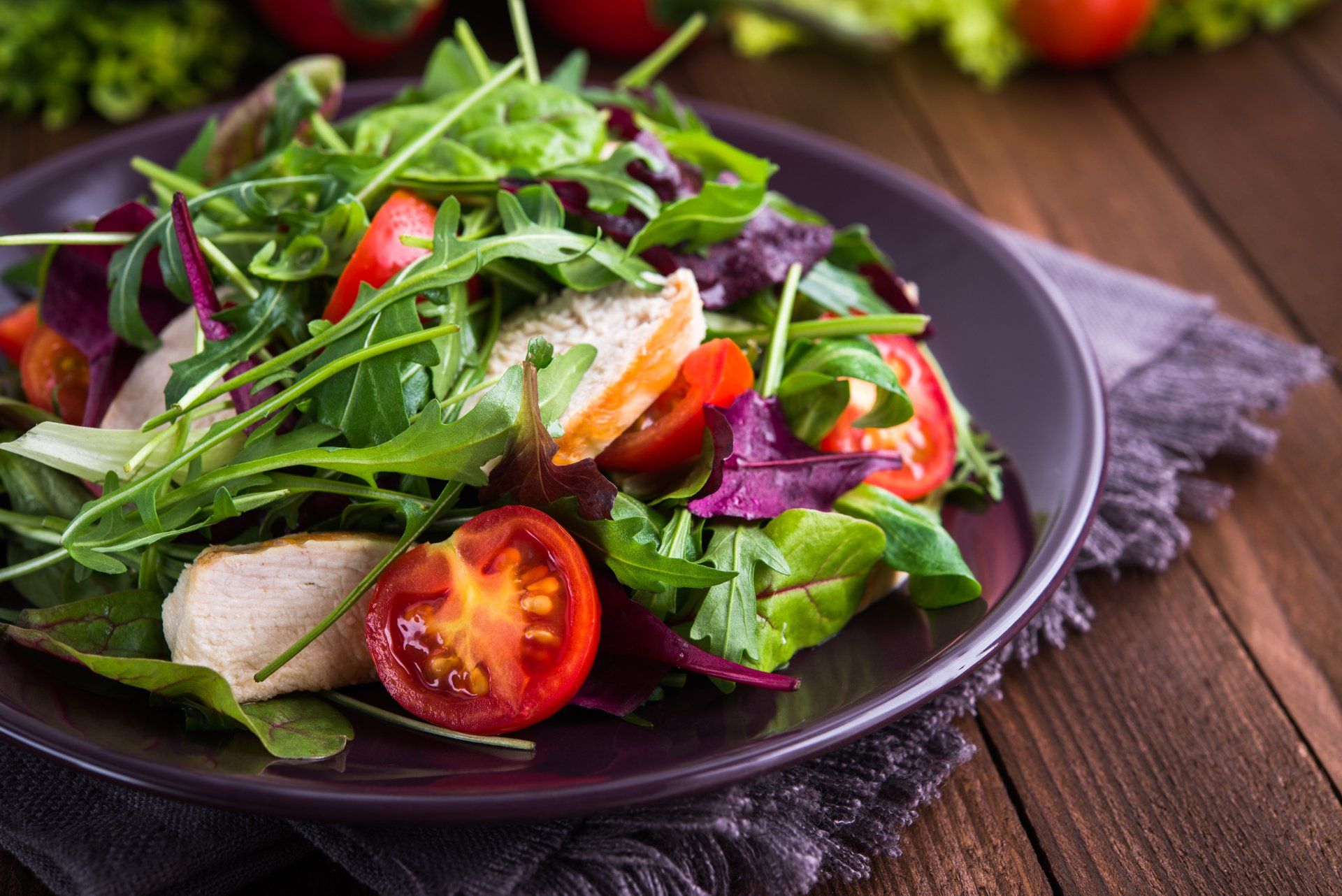 Fresh salad with chicken, tomatoes and mixed greens (arugula, mesclun, mache) on wooden background close up. Healthy food.