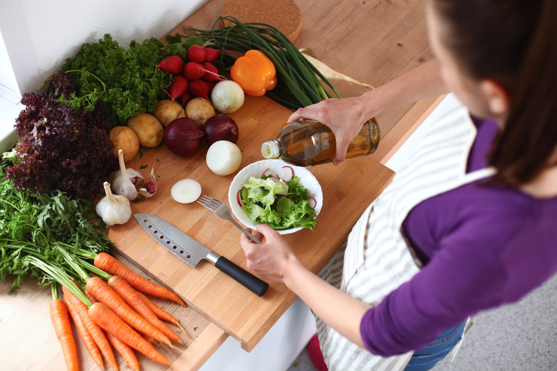 Young woman mixing fresh salad, oil recharge.