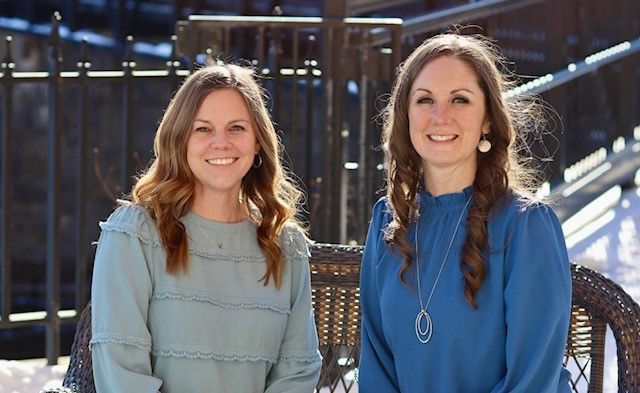 Two women in blue shirts are sitting next to each other on a chair.