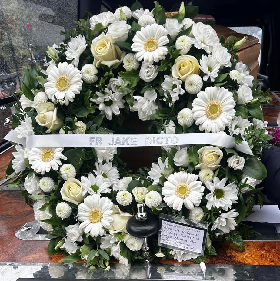 A wreath of white daisies and roses is on a coffin.