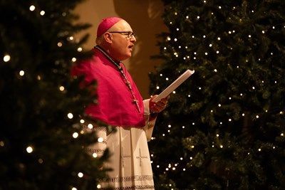 Archbishop John Wilson standing in front of a christmas tree .