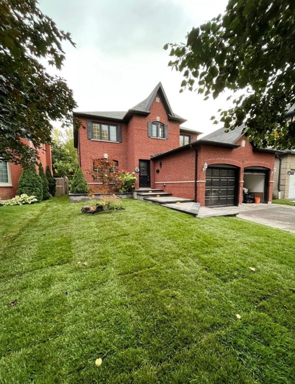 A two-story red brick house with a steep roof, dark garage doors, and a freshly sodded green lawn under a cloudy sky.