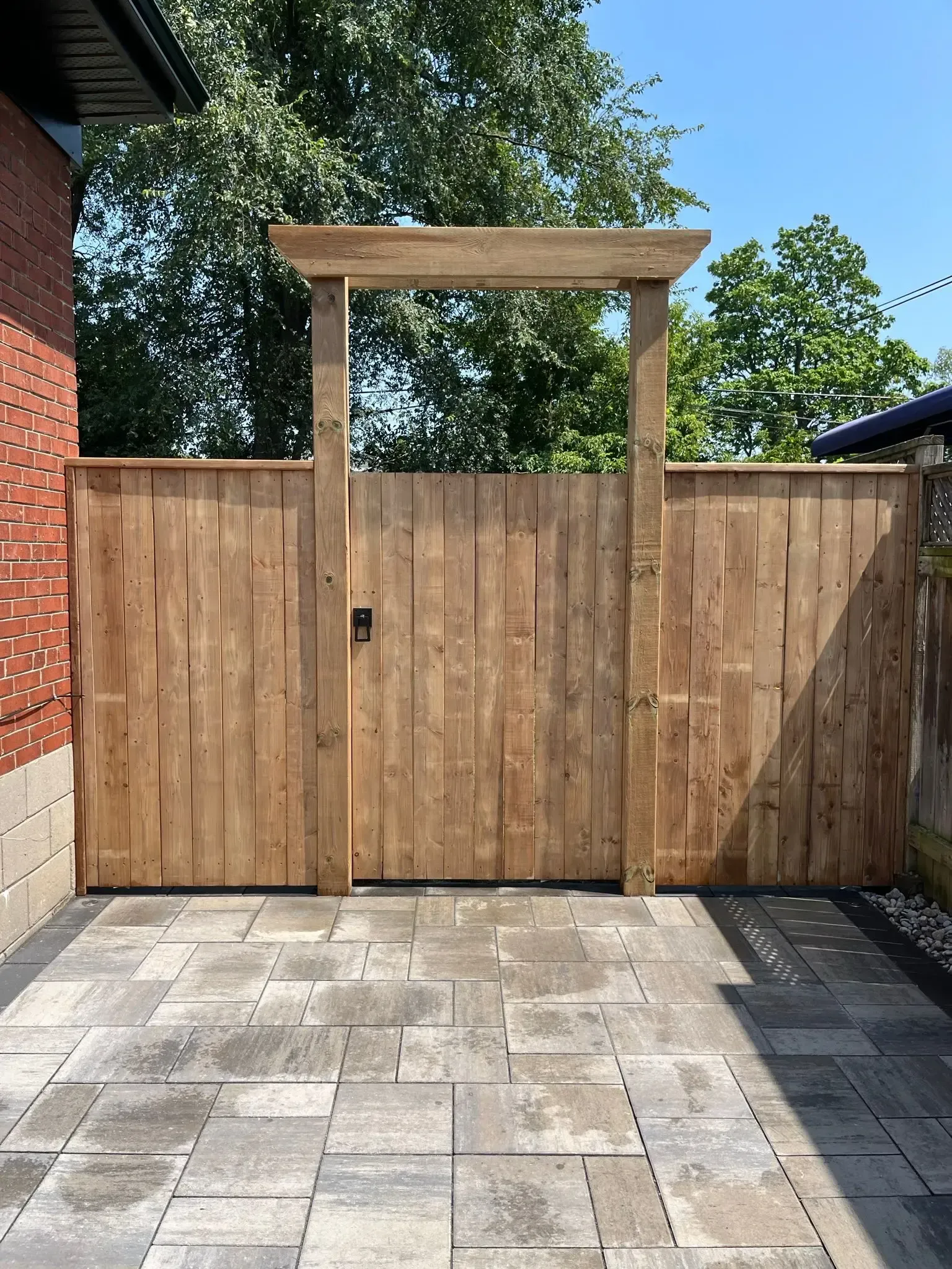 Wooden gate and fence with an archway. Brick building on the left, grey paving stones in front.