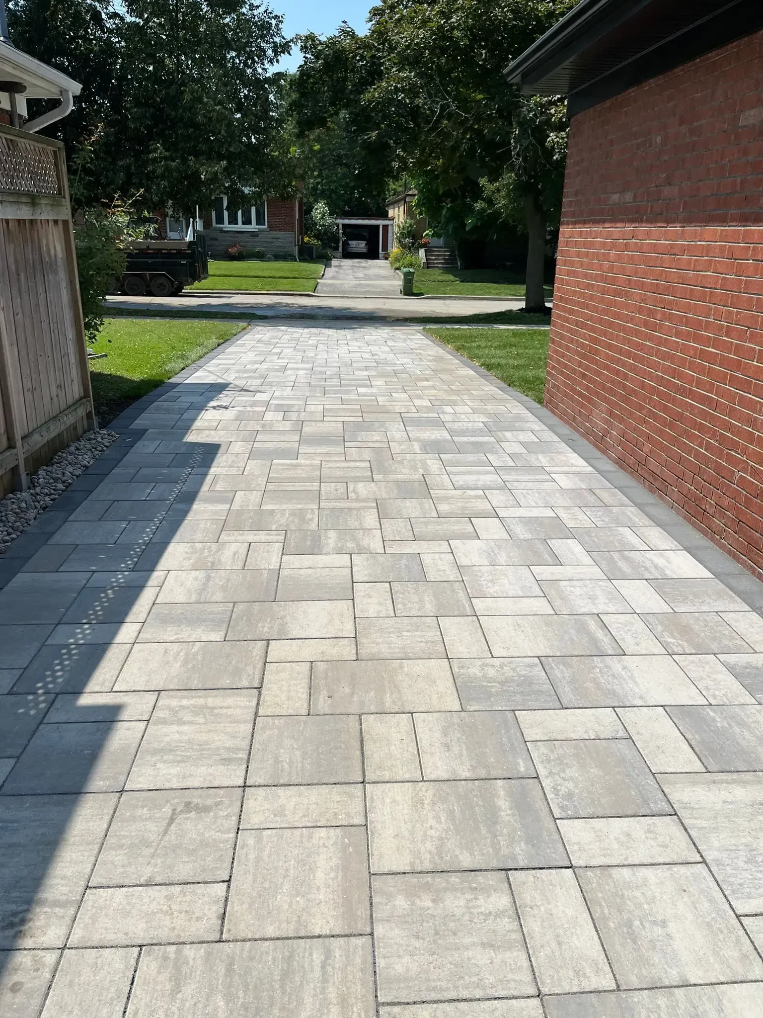 Stone paver driveway leading towards a red brick building and a residential street, under sunlight.