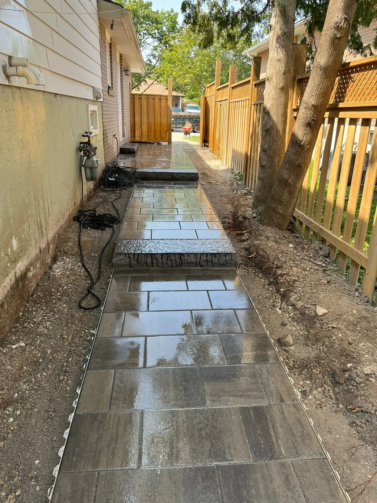 A paved walkway with steps alongside a building and fence on a sunny day.