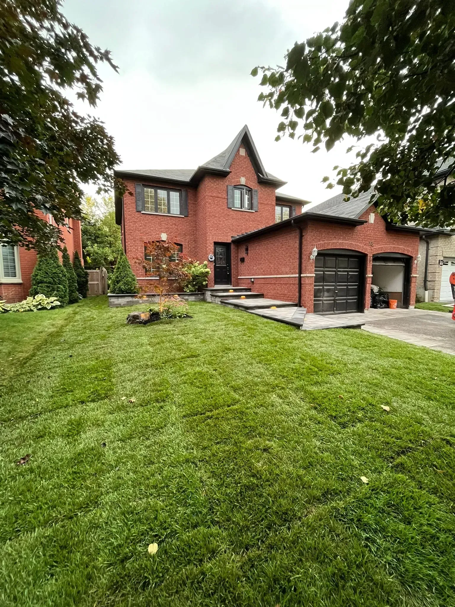 Brick house with a two-car garage, green lawn, and cloudy sky.